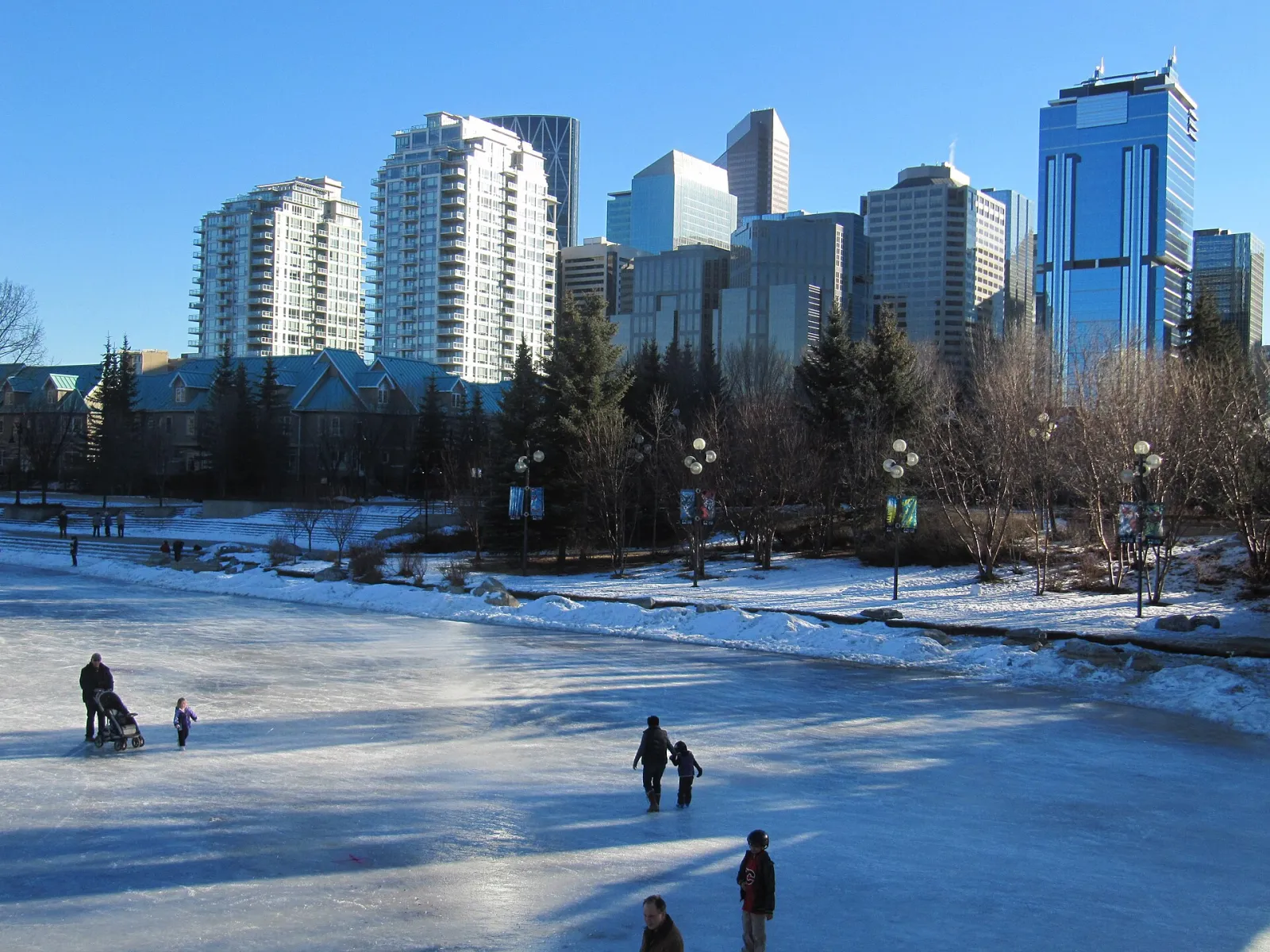 Patinadores en el hielo de la laguna de Prince's Island con las torres del centro de Calgary al fondo, en un día despejado de invierno — Prince's Island Park Outdoor Skating Rink