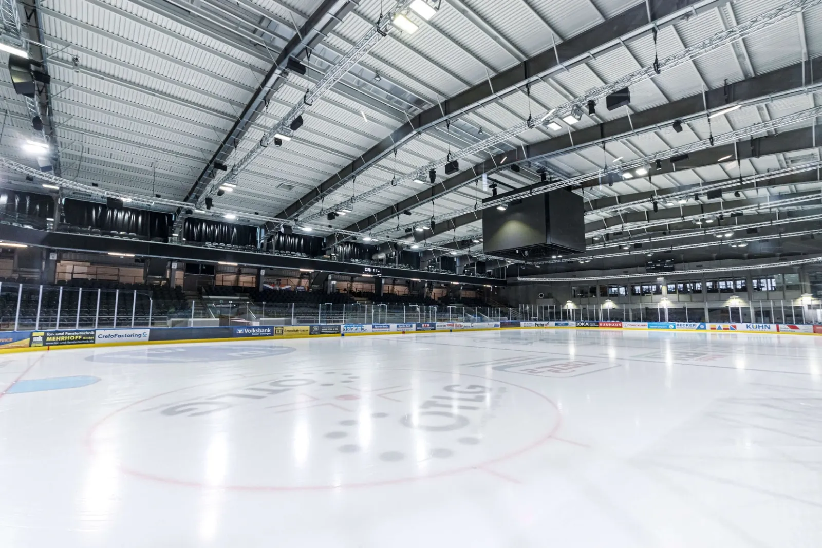 The empty Kassel ice surface under the arena roof, with the boards, glass and banked seating around it. — Probonio Arena (Eissporthalle Kassel)