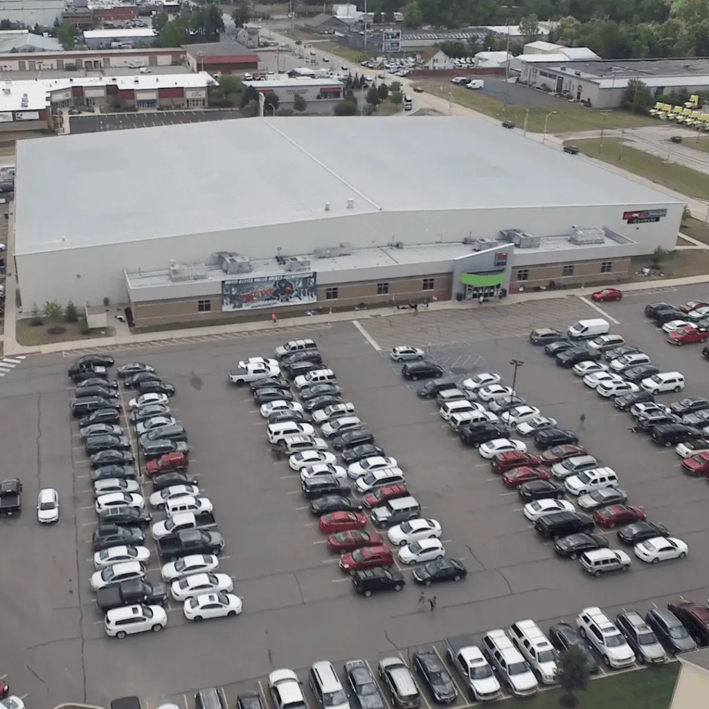 Aerial drone view of the PSM Icehouse building, showing its low white roof, entrance canopy and parking lot in Fort Wayne. — SportONE Parkview Icehouse (PSM Icehouse)