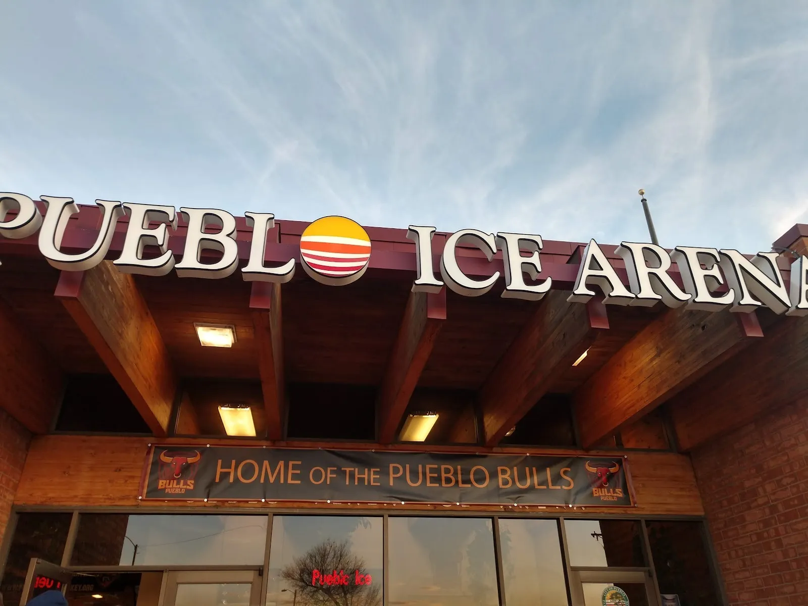 La fachada de Pueblo Ice Arena, con su nombre en letras grandes sobre una marquesina de vigas de madera y una manta de Home of the Pueblo Bulls — Pueblo Ice Arena