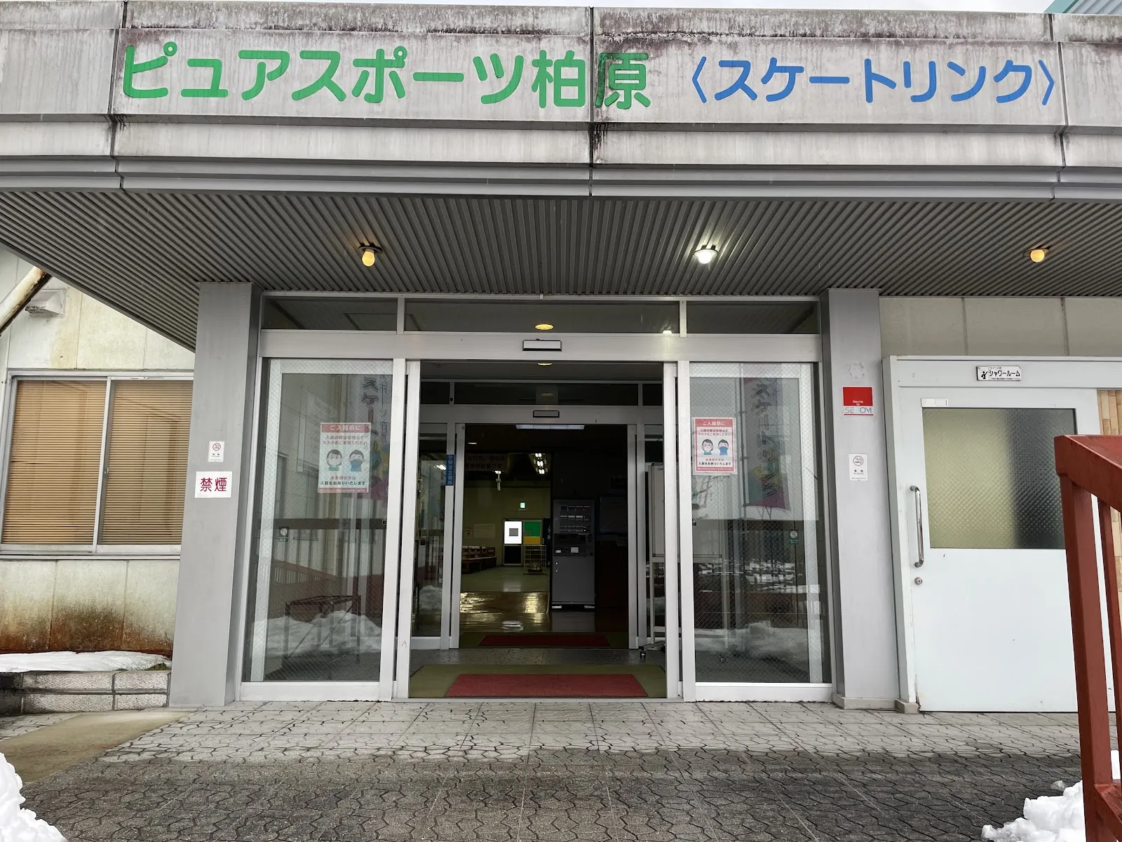 The glass entrance of Pure Sports Kaibara with the green "Pure Sports Kaibara (Skating Rink)" sign above the doors and snow banked beside the steps. — Pure Sports Kaibara Skate Rink