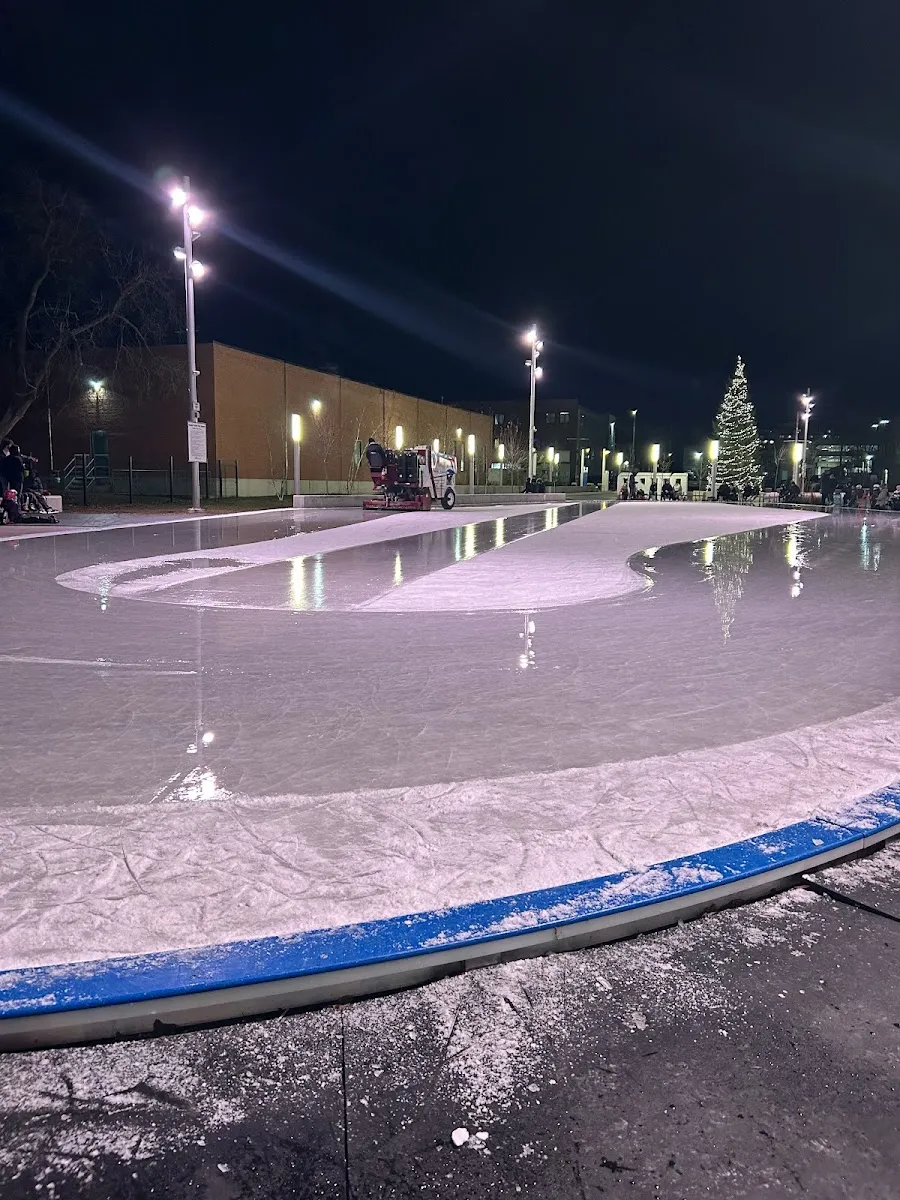 La pista iluminada de Quaker Foods City Square en Peterborough de noche, con la máquina alisadora en el lado opuesto y un árbol decorado más allá — Quaker Foods City Square Outdoor Rink