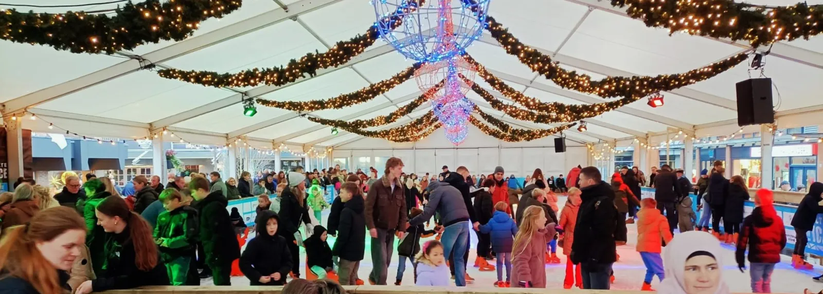 Public skating under the tent roof of Raalte on Ice, with a crowd of skaters on the ice; skaters at distance. — Raalte on Ice