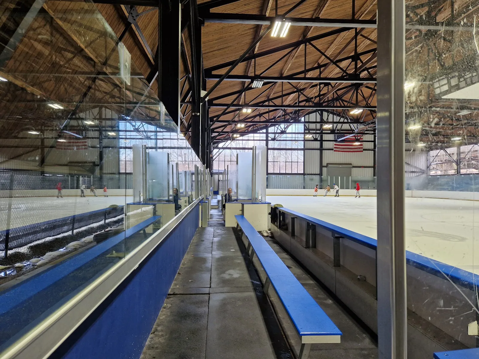 El hielo de Ralph Walker Ice Rink visto a lo largo del cristal y las bancas bajo las armaduras de madera del techo, con unos cuantos patinadores al otro lado de la pista — Ralph Walker Ice Rink