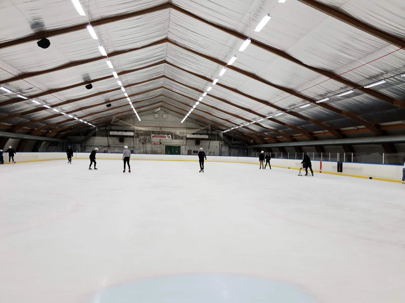 Skaters far across the ice of Rambergsrinken under its barrel-vaulted roof — Rambergsrinken