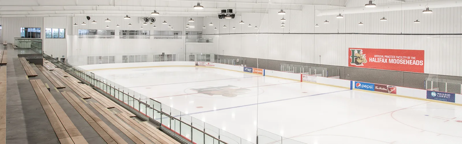 Una pista vacía dentro del RBC Centre con bancas de madera para espectadores a lo largo de las vallas y una manta roja que dice 'Official Practice Facility of the Halifax Mooseheads'. — RBC Centre