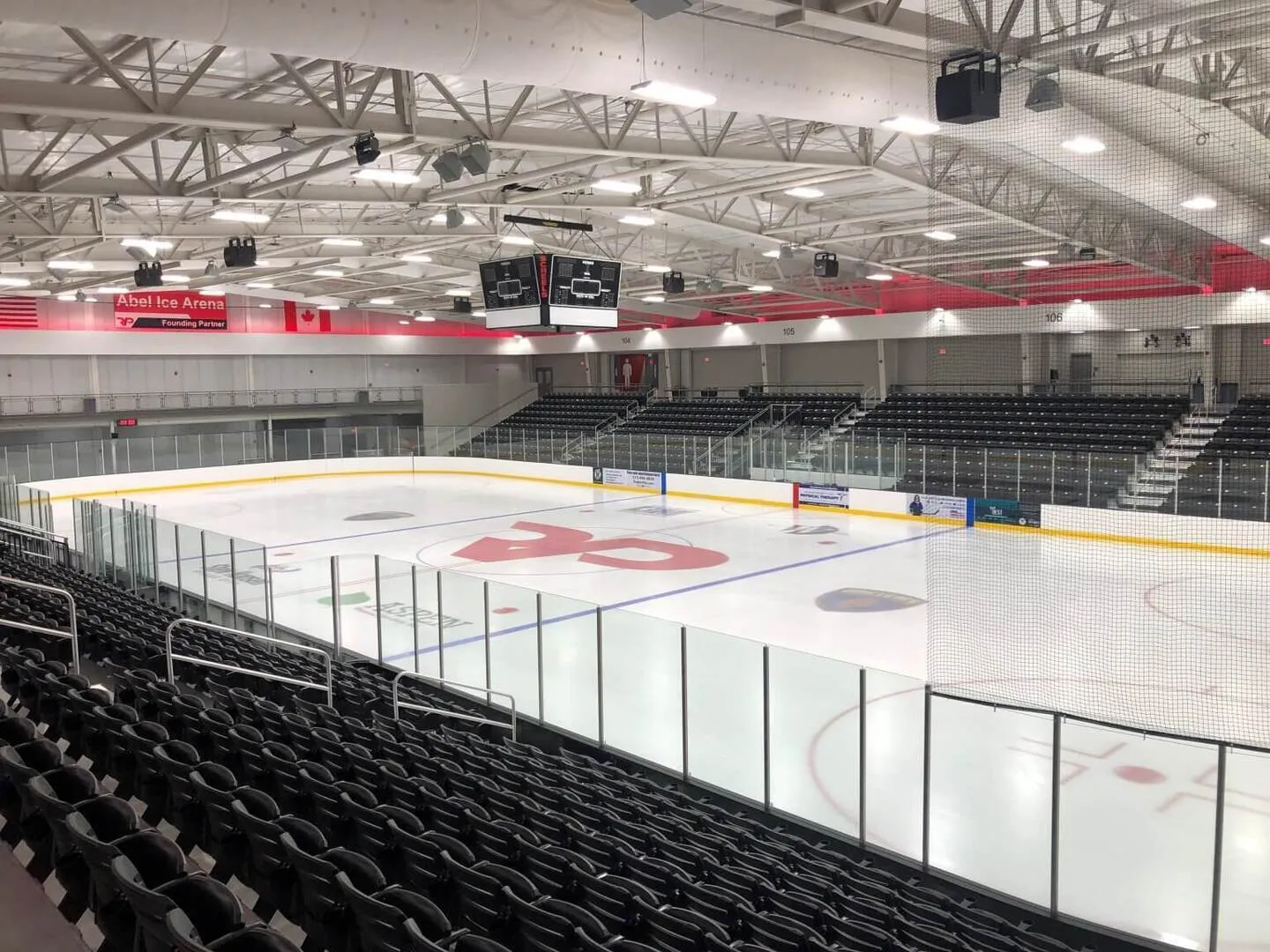 Abel Ice Arena at RecPlex: full ice sheet from an upper corner, empty stadium-style seating on both long sides, red RP logo at center ice, "Abel Ice Arena / Founding Partner" signage above the seating. — MidAmerican Energy Company RecPlex