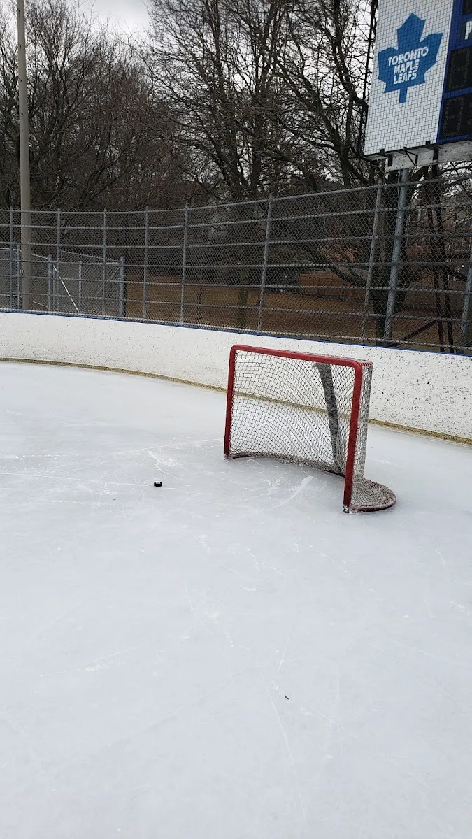 A hockey net, puck, boards and the scoreboard at the Rennie Park rink, with no people in view — Rennie Park Outdoor Ice Rink and Skate Trail