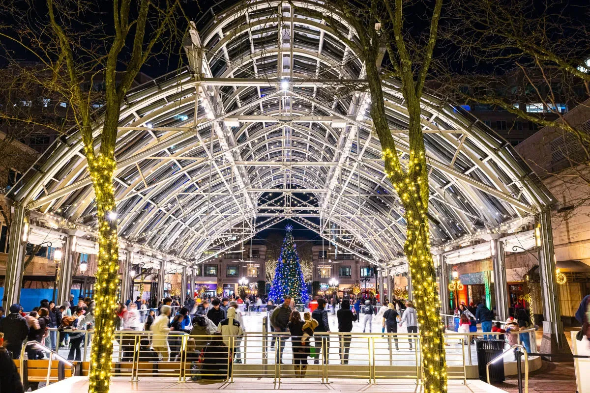 El pabellón de cristal de Reston Town Center, iluminado de noche, con patinadores en la pista — Reston Town Center Pavilion Ice Rink