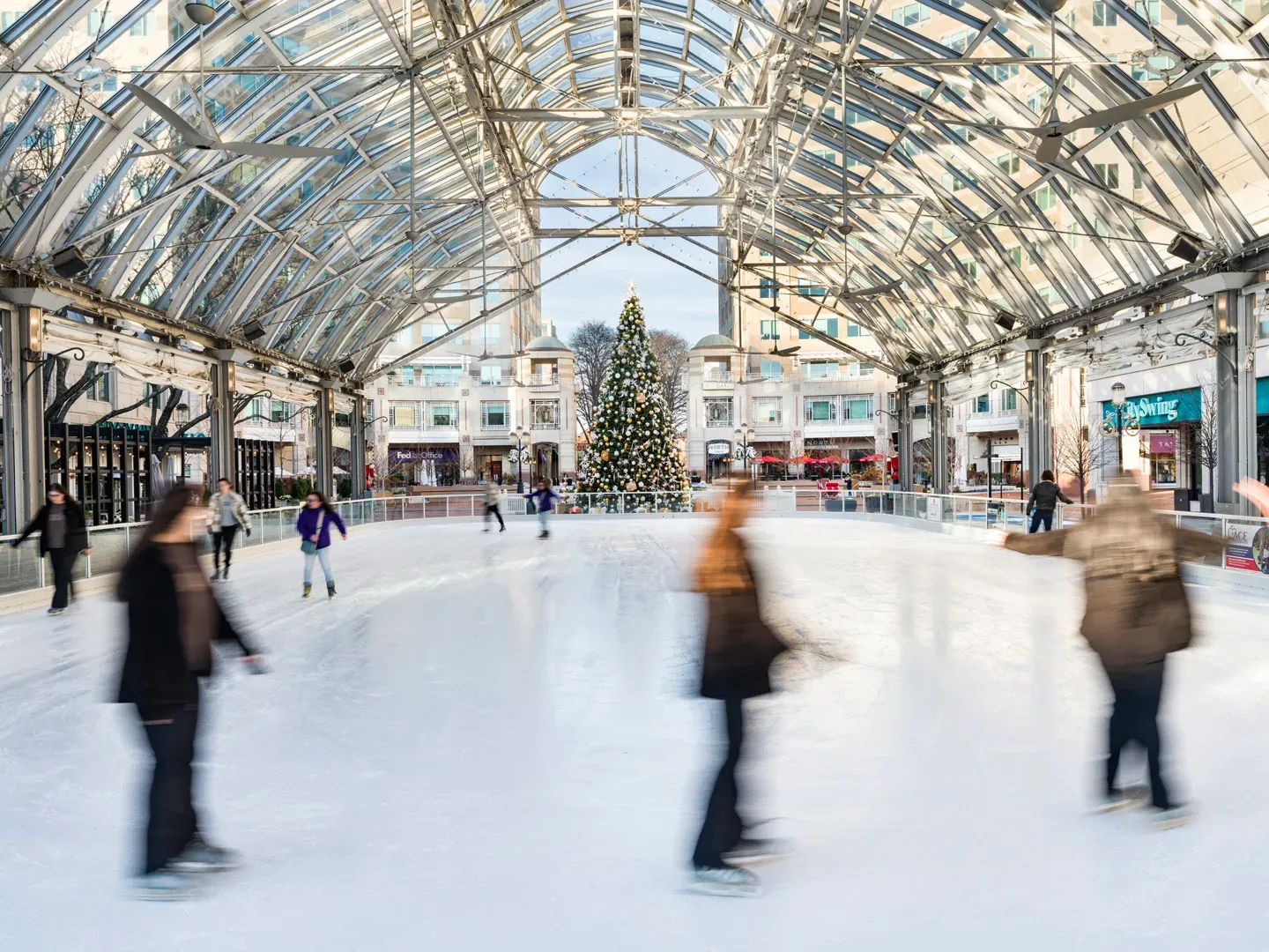 Patinadores en movimiento sobre el hielo bajo el techo de cristal del pabellón de Reston Town Center — Reston Town Center Pavilion Ice Rink