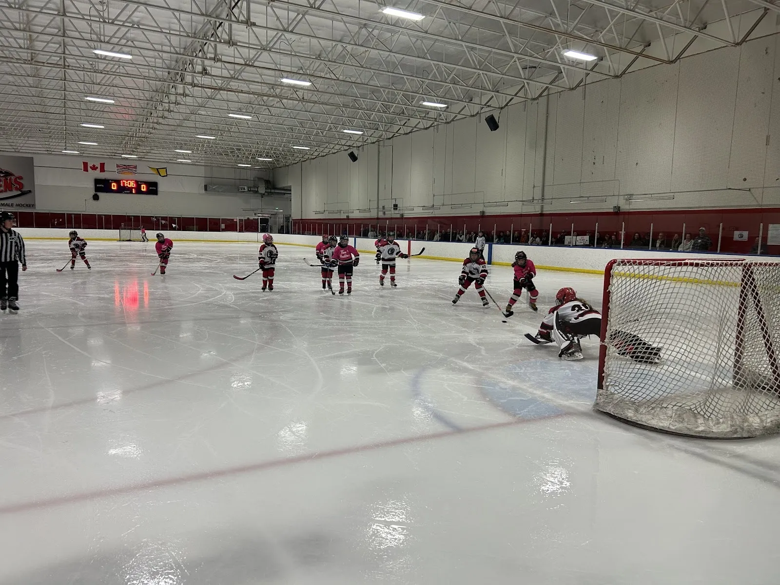 A game seen along the boards of a wide sheet, players spread across the ice behind a net with a high steel roof overhead. — Richmond Ice Centre