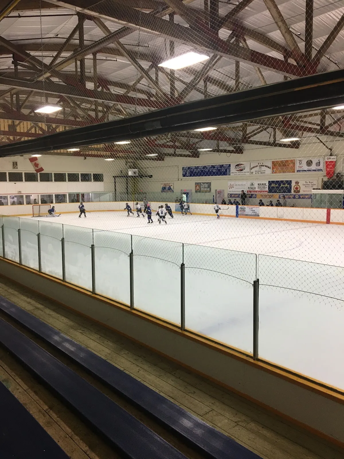 A game under way at the far end of the ice at Ridgetown Arena, seen along the glass and boards from the stands beneath the steel roof trusses. — Ridgetown Arena (East Kent Memorial Arena)