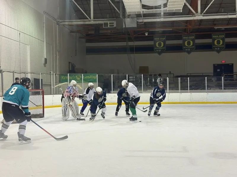 A scrimmage on the ice at Lane Ice Center, players gathered near a net under an exposed steel roof with Oregon banners hung along the far wall. — The Rink Exchange (Lane Ice Center)