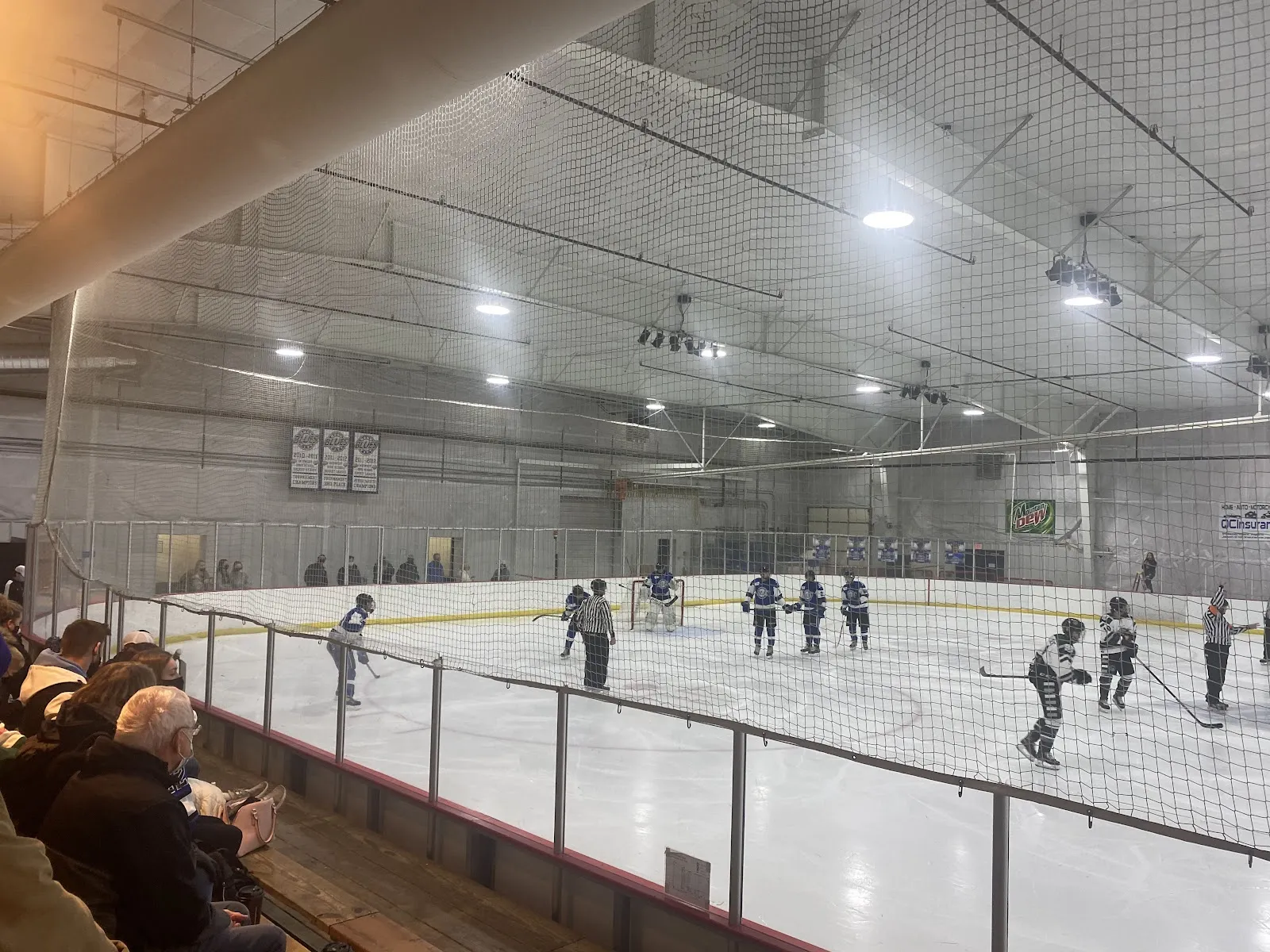 A youth hockey game on the ice at The River's Edge seen from the stands, players at a distance — The River's Edge Ice Arena