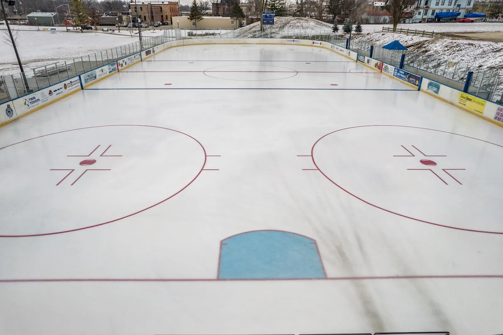 The outdoor NHL-size ice surface at Riverside Ice Arena with boards and sponsor signs. — Riverside Ice Arena