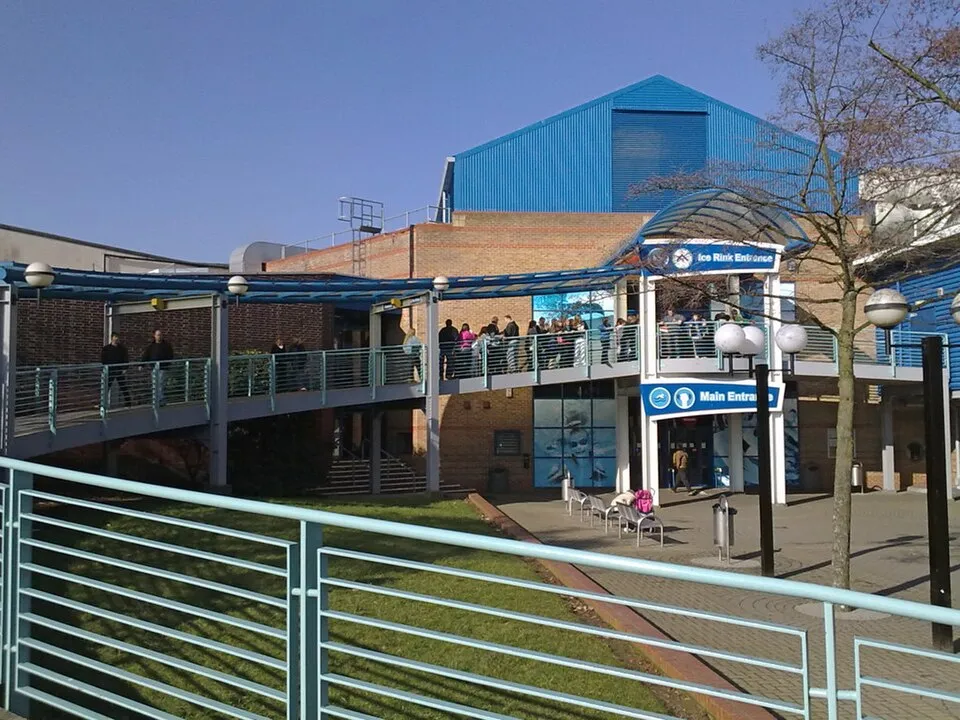 The entrance side of Riverside Ice and Leisure Centre in Chelmsford, with the blue-roofed ice hall behind a brick frontage and a covered walkway signed Ice Rink Entrance and Main Entrance. — Riverside Ice Rink (Riverside Leisure Centre), Chelmsford