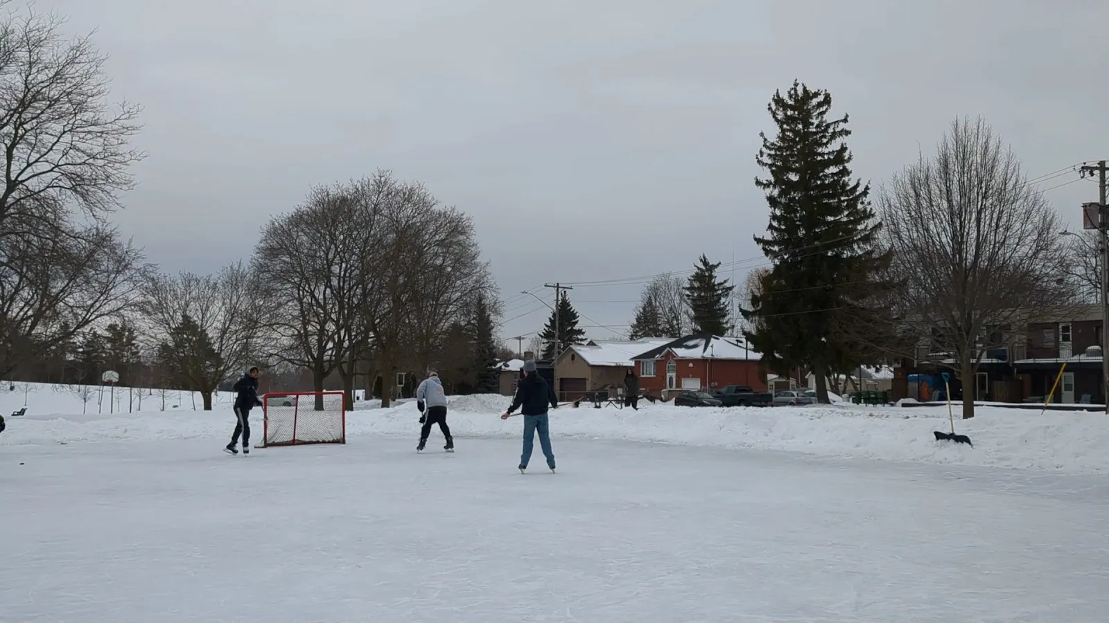 Un juego de hockey libre en la pista comunitaria nevada de Riverview Park en Lindsay, con una portería, bancos de nieve y casas detrás — Riverview Park Outdoor Rink