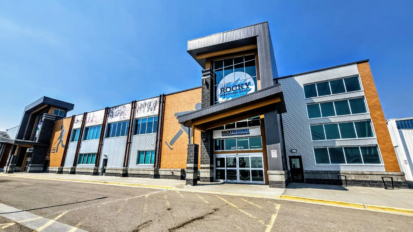 The entrance of the Rocky Regional Recreation Centre under a blue sky, with the glazed entrance tower, the Rocky sign and the brick-and-metal front of the building. — Rocky Regional Recreation Centre