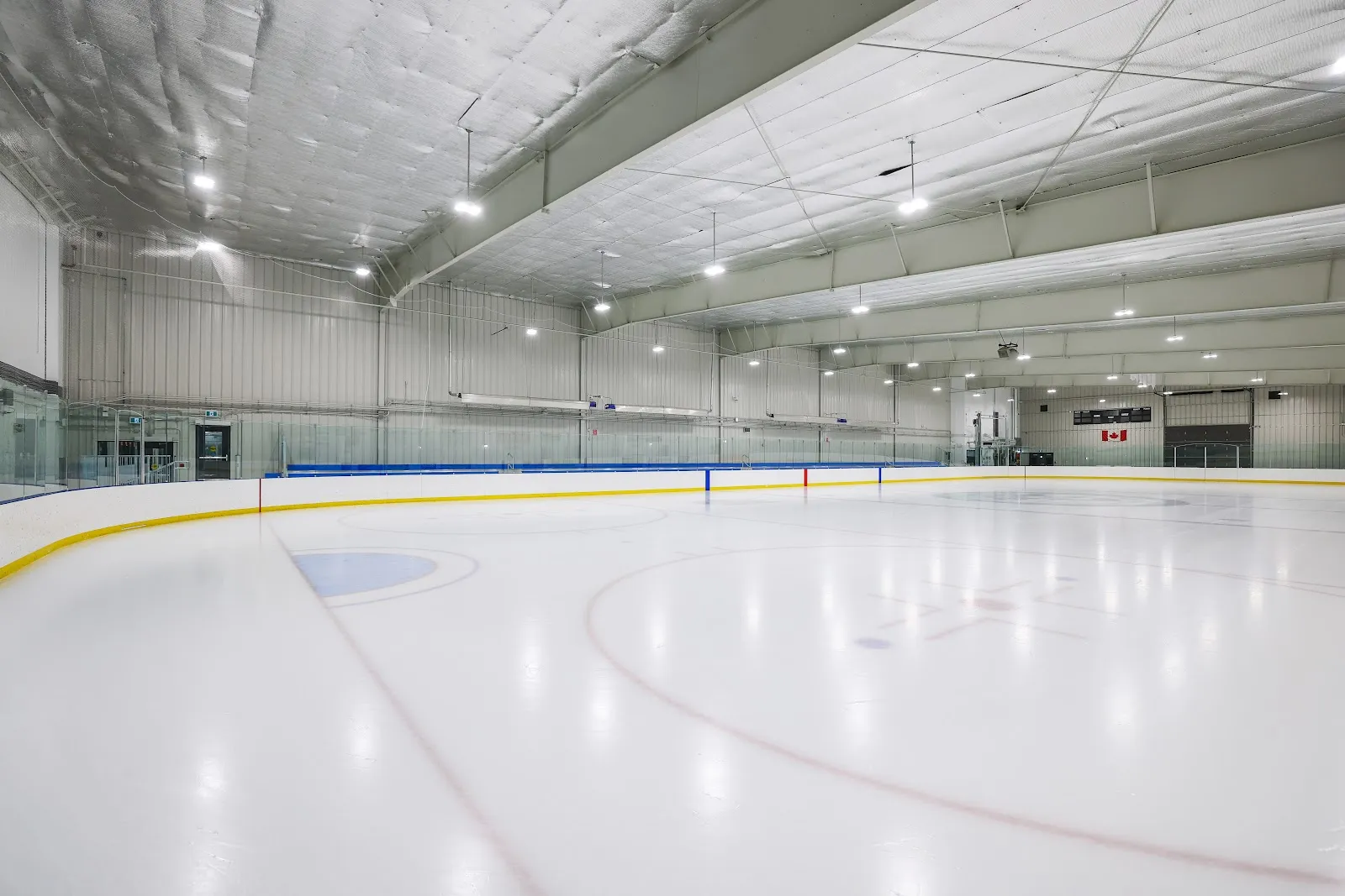 An empty NHL-size ice sheet with the yellow board rail, blue line and face-off circle under the arena's bright overhead lights. — Ron Ebbesen Twin Arena