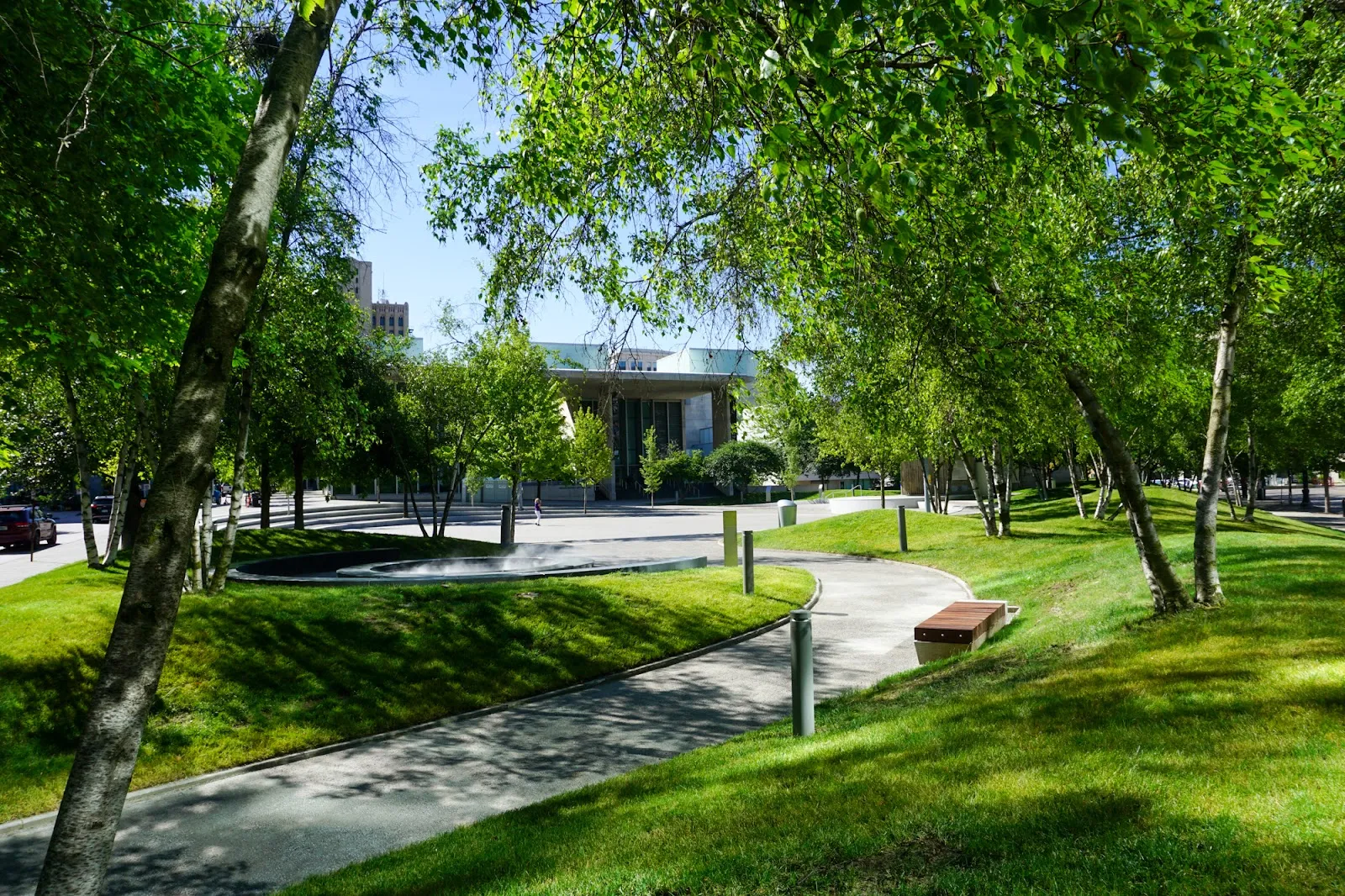 Rosa Parks Circle in summer, with the curved walk and the sunken circle under birch trees and the downtown plaza building beyond. — Rosa Parks Circle Ice Rink