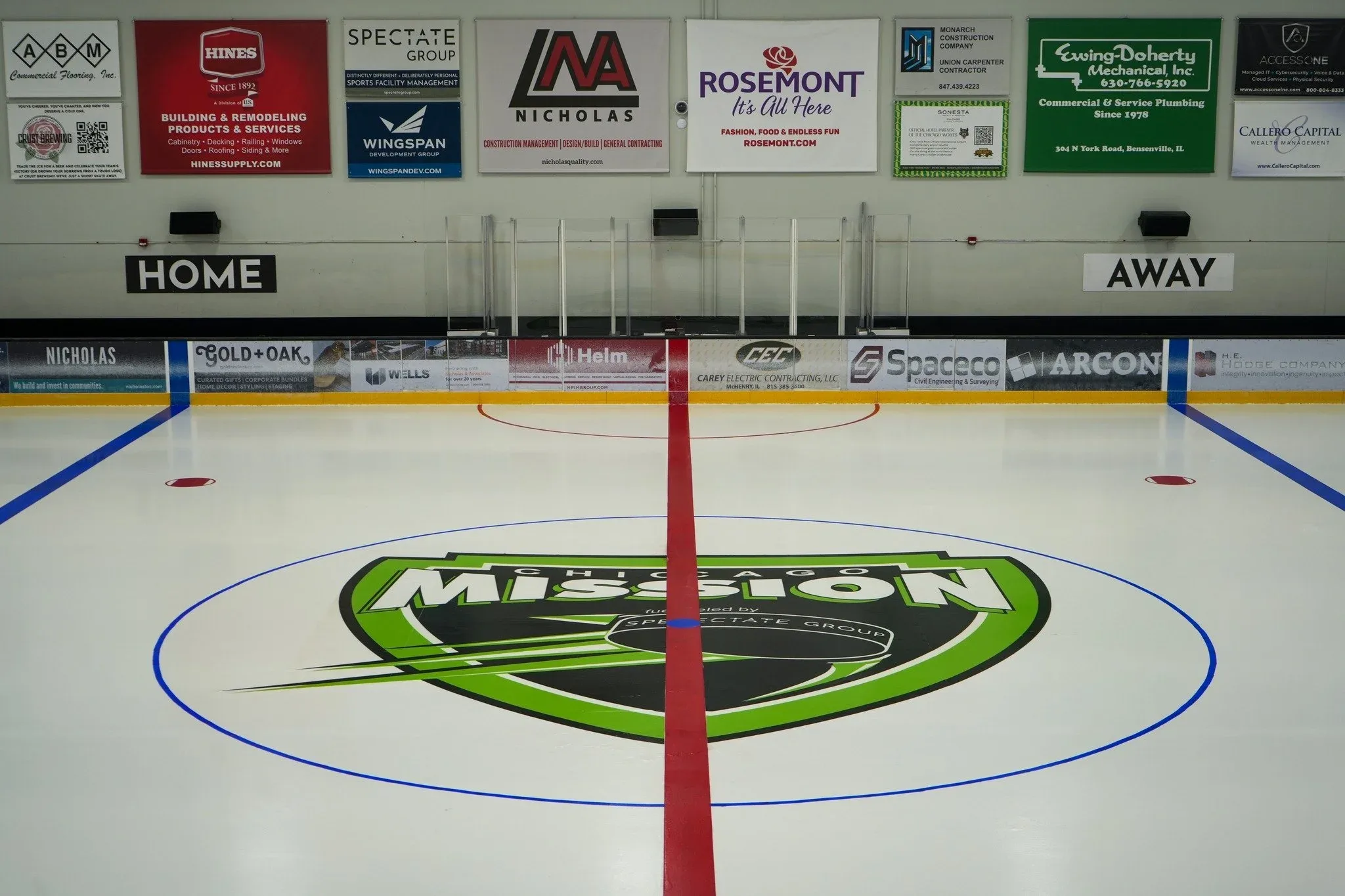 Logotipo de Mission en el centro de la pista y los anuncios de patrocinadores a lo largo de la pared del fondo — Rosemont Ice Arena
