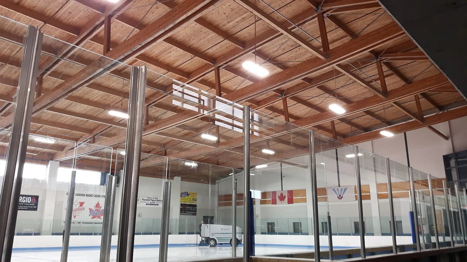 The ice at Rosemount Community Centre in Thornhill seen through the glass under an exposed timber roof, with the resurfacer parked at the far end — Rosemount Community Centre (Vaughan)