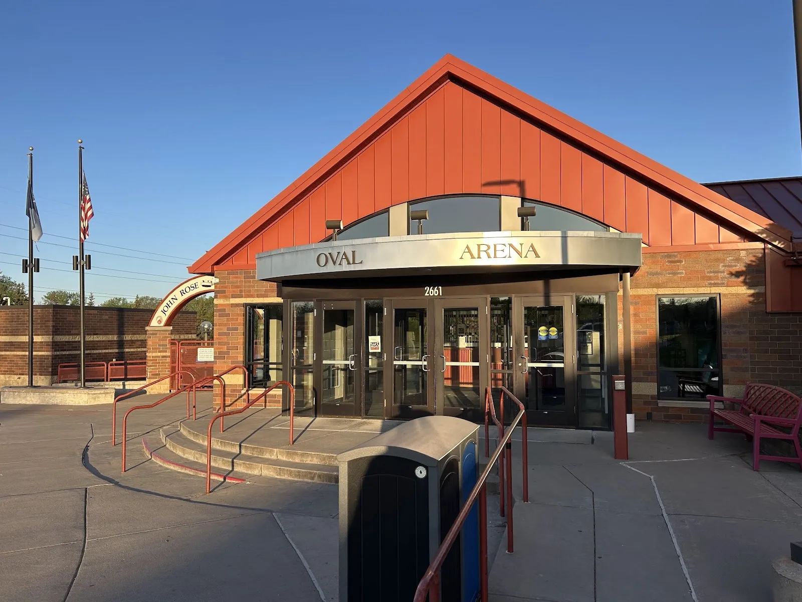 The red-roofed brick entrance of the Roseville Skating Center with a glazed doorway under an Arena sign, seen from the plaza at dusk. — Roseville Parks and Recreation