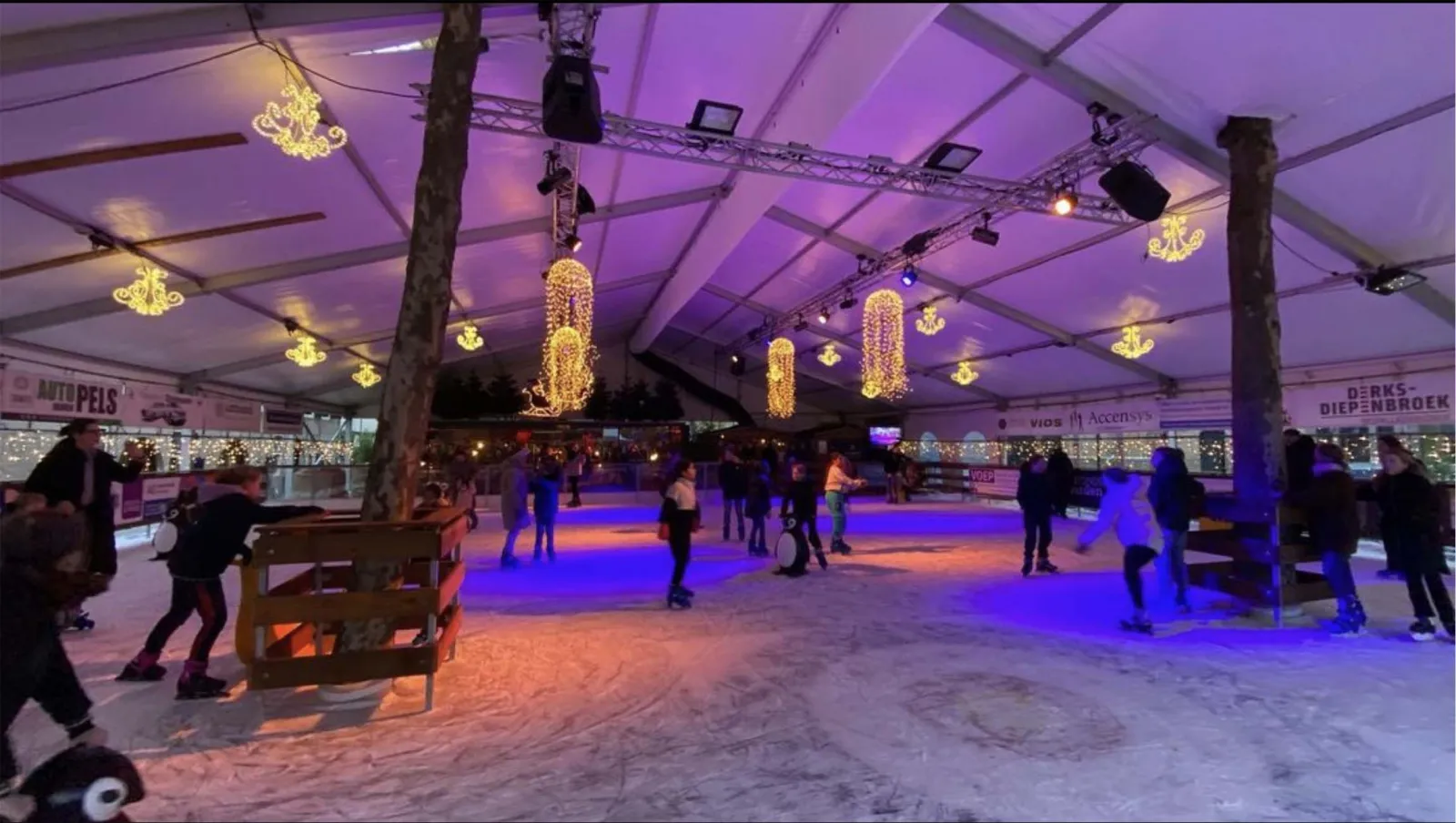 The covered Rotary-ijsbaan on the Kerkplein in Woerden, lit in purple, with skaters at distance on the artificial ice. — Rotary-ijsbaan Woerden