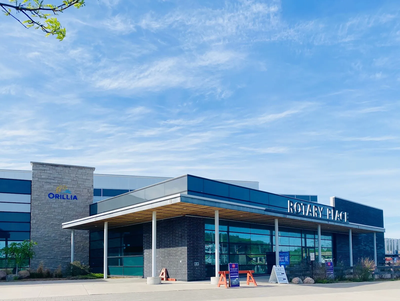 The Rotary Place entrance canopy with the name lettered above the glass and an Orillia sign on a stone pillar at left. — Rotary Place (Orillia)