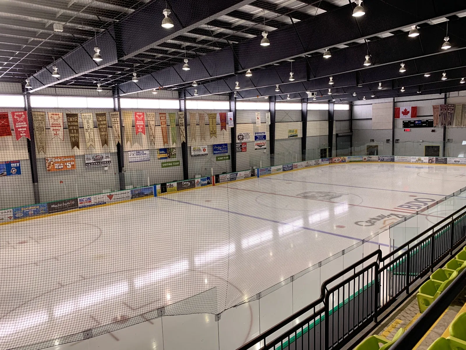 An empty pad seen over the glass from the stands, with championship banners hanging along the far wall. — Rotary Place (Orillia)