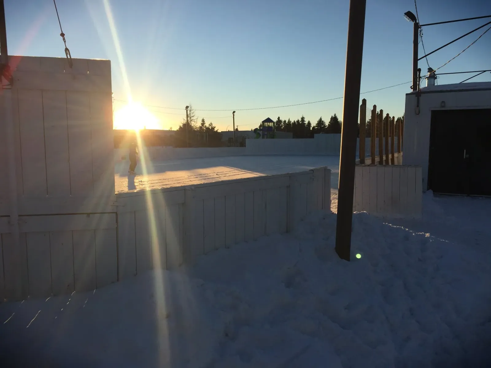 Snow-lined boards at the Royal Gardens community rink at sunrise, with the rink building beyond — Royal Gardens Community League Rink