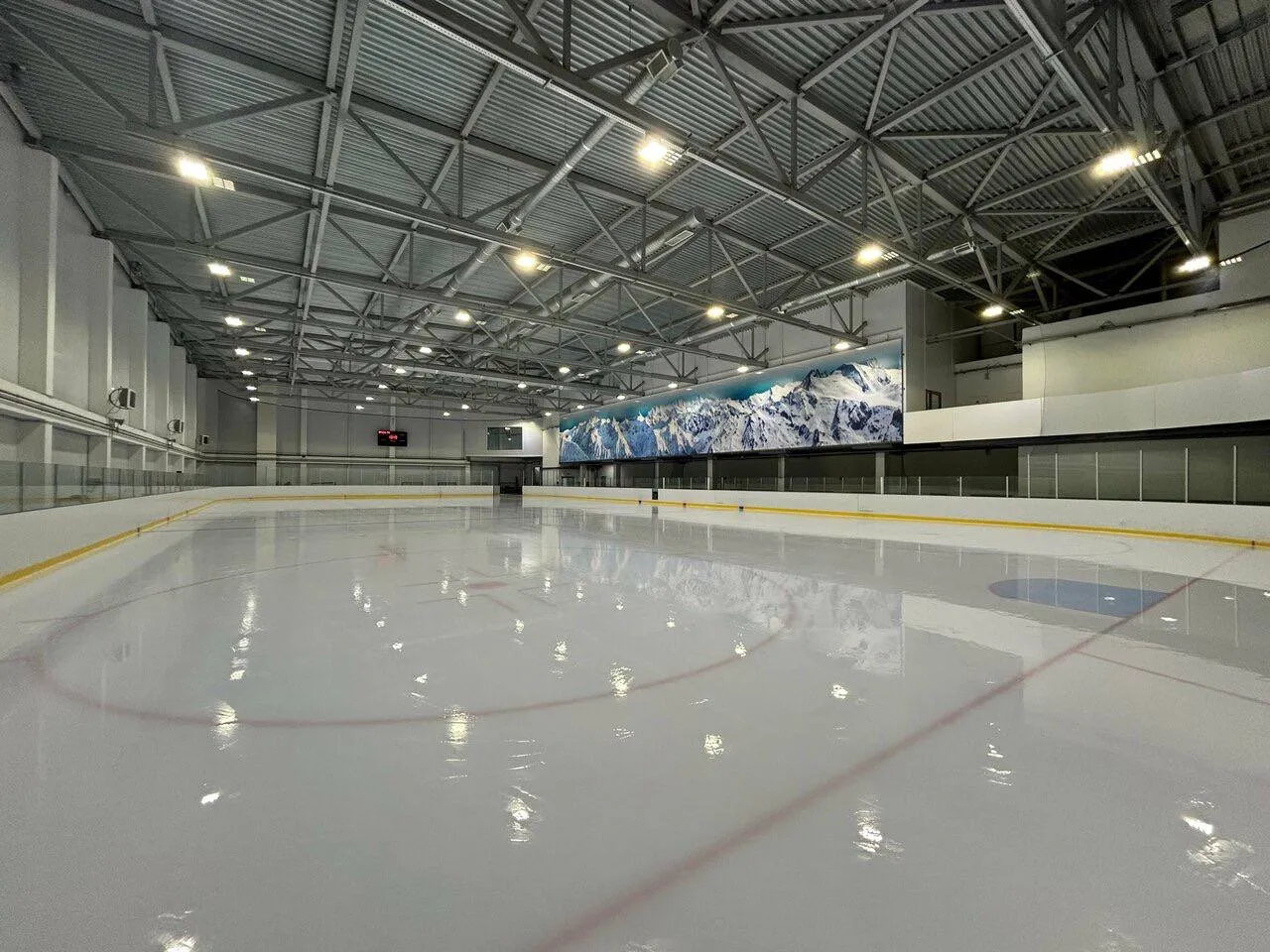 The empty ice sheet inside the Rubezh arena, with the mountain mural above the boards (Google Maps listing photo, read 2026-10-19) — Rubezh Ice Arena Saint Petersburg