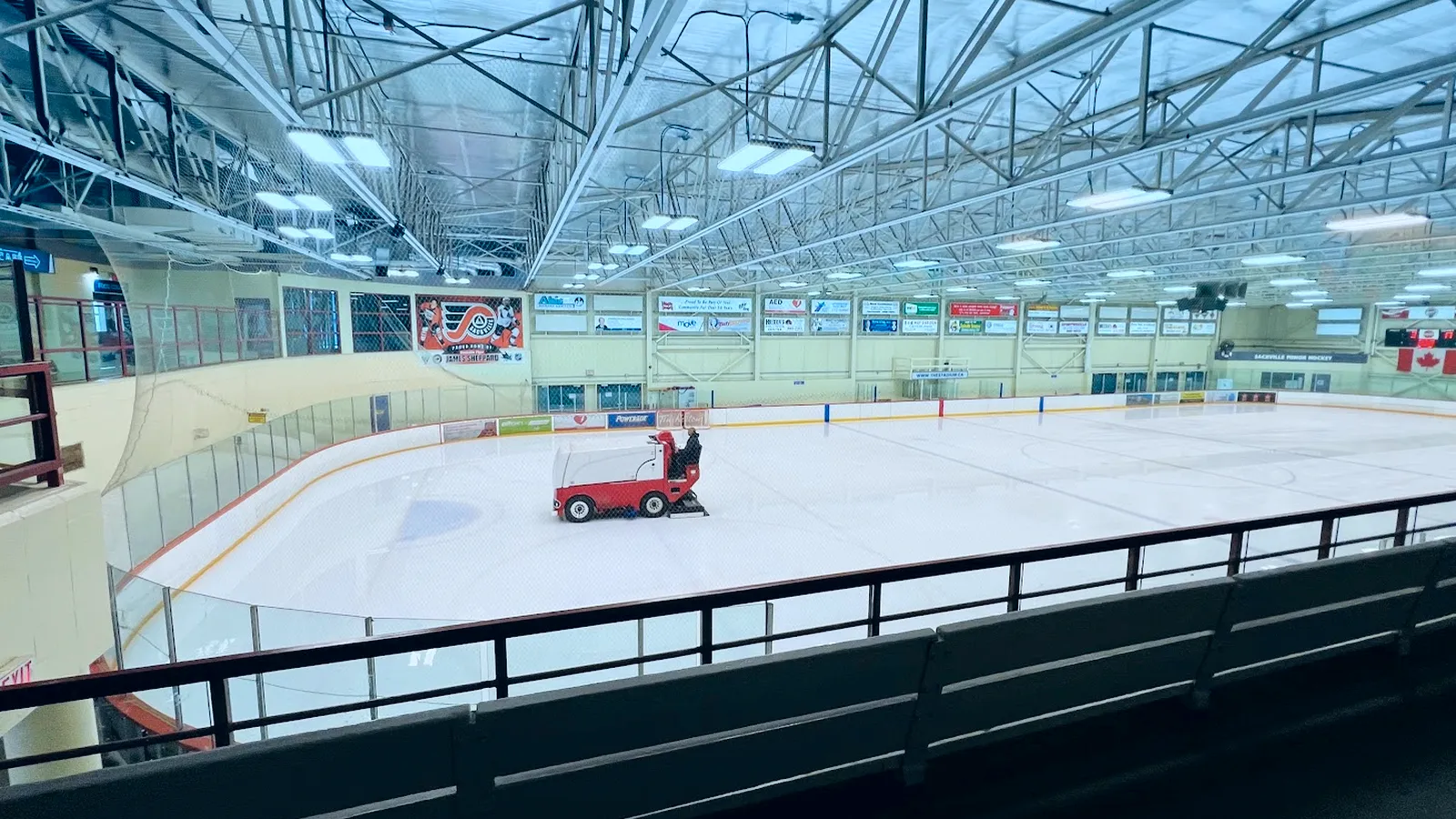 The arena ice at the Sackville Sports Stadium with the resurfacer at work, seen from the upper rail under the steel roof trusses. — Sackville Sports Stadium
