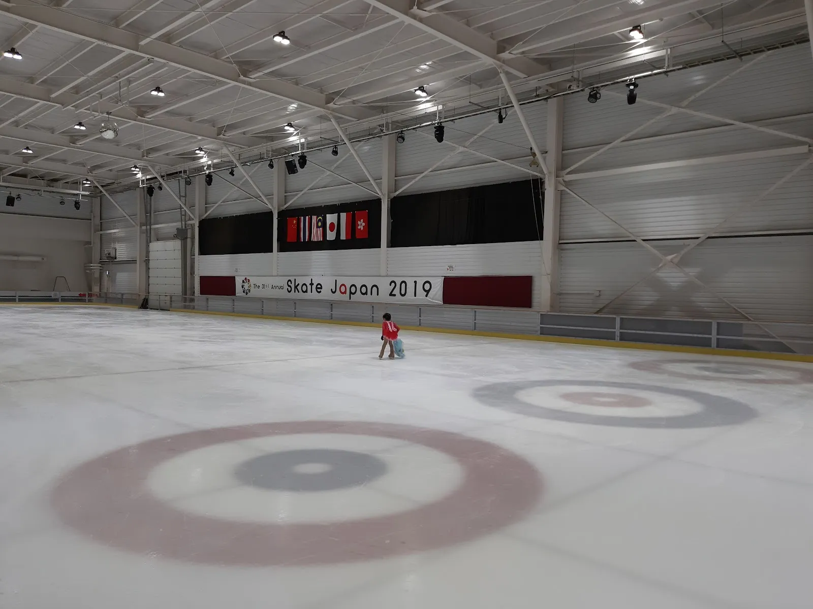 The ice of Saitama Ice Arena in Ageo, with painted curling rings, a Skate Japan 2019 banner on the far wall and one small skater in the distance — Saitama Ice Arena