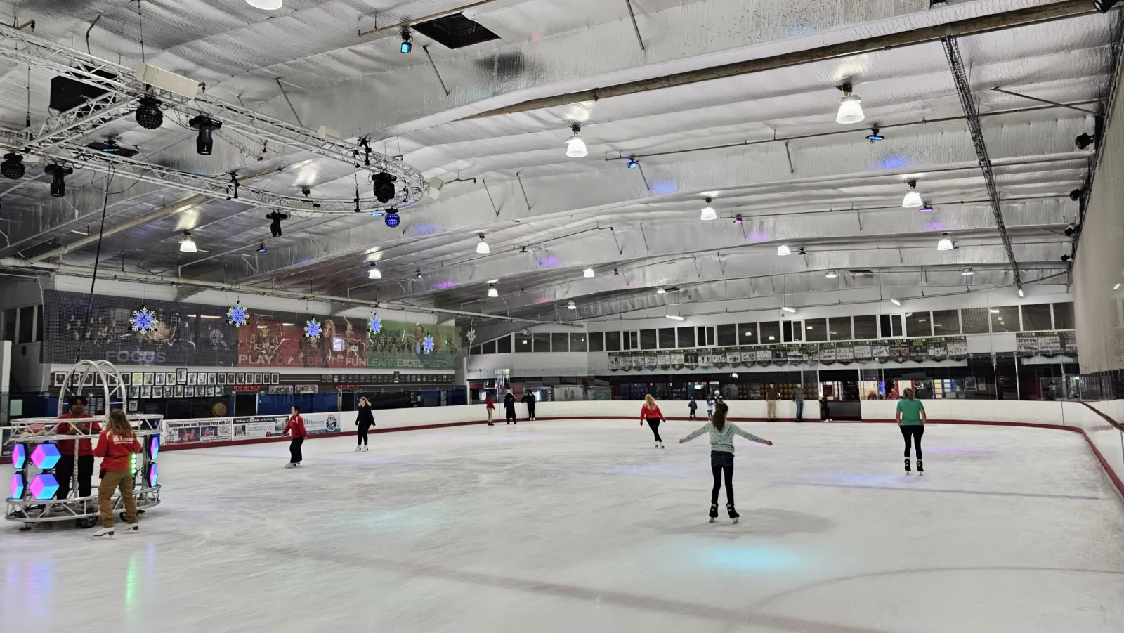 Un patinaje público visto desde las vallas, con patinadores en el hielo, una cabina de DJ a la izquierda y las ventanas de observación a lo largo del lado opuesto. — San Diego Ice Arena