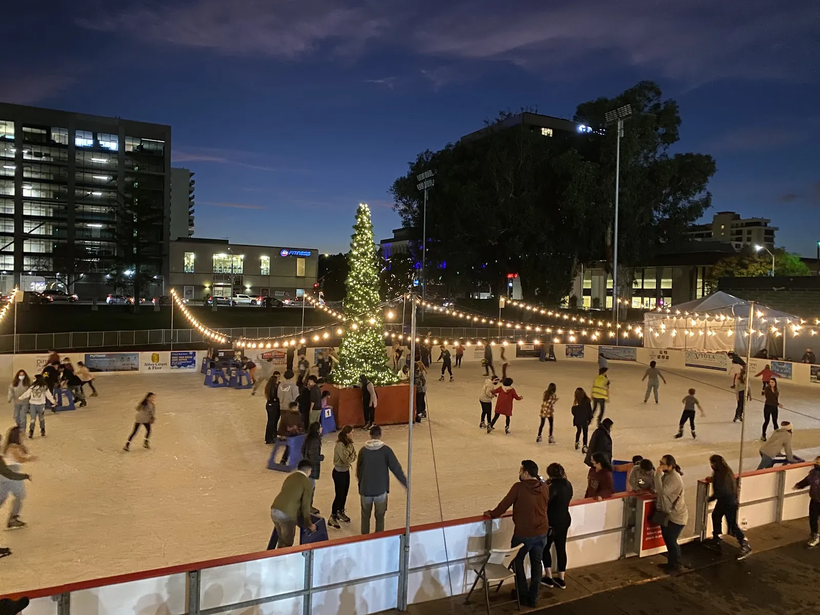 La pista San Mateo On Ice al atardecer, con un árbol navideño y tiras de luces en Central Park (foto del listado de Google Maps) — San Mateo On Ice