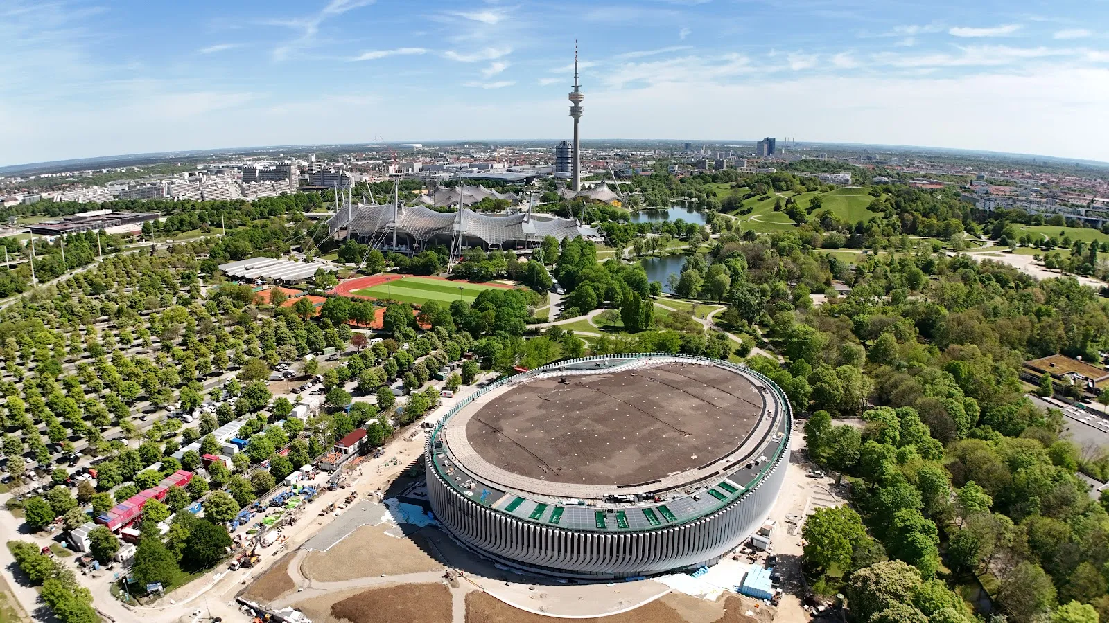 Luftbild der runden SAP-Garden-Arena im Norden des Olympiaparks, dahinter der Park und der Olympiaturm. – SAP Garden Eispark