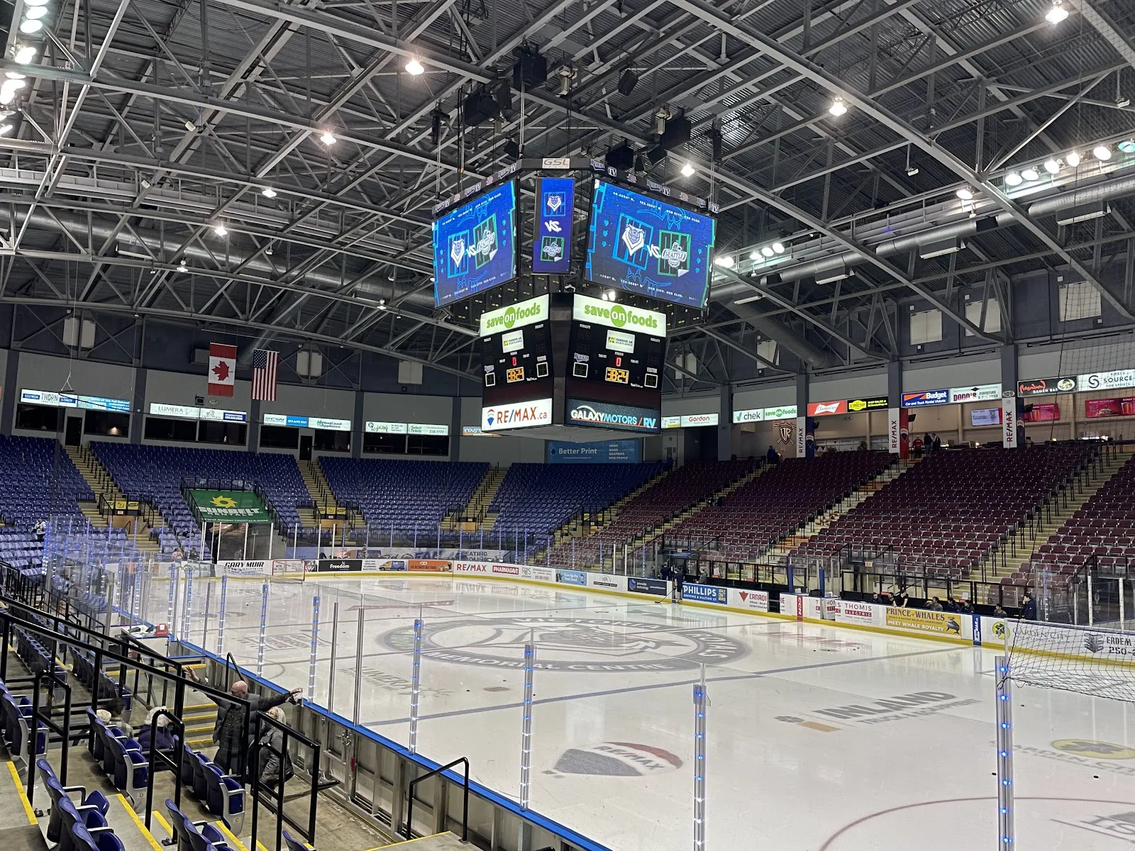 The arena bowl at the Save-On-Foods Memorial Centre seen from the stands, with the ice, boards, banners and a four-sided scoreboard overhead. — Save-On-Foods Memorial Centre