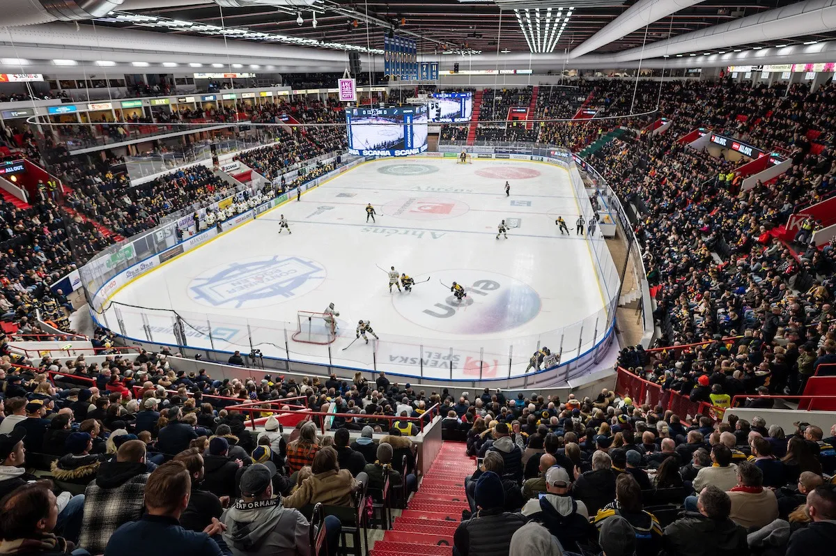 En fullsatt Scaniarinken under en ishockeymatch, spelare över rinken och åskådare som fyller de röda läktarna. – Scaniarinken