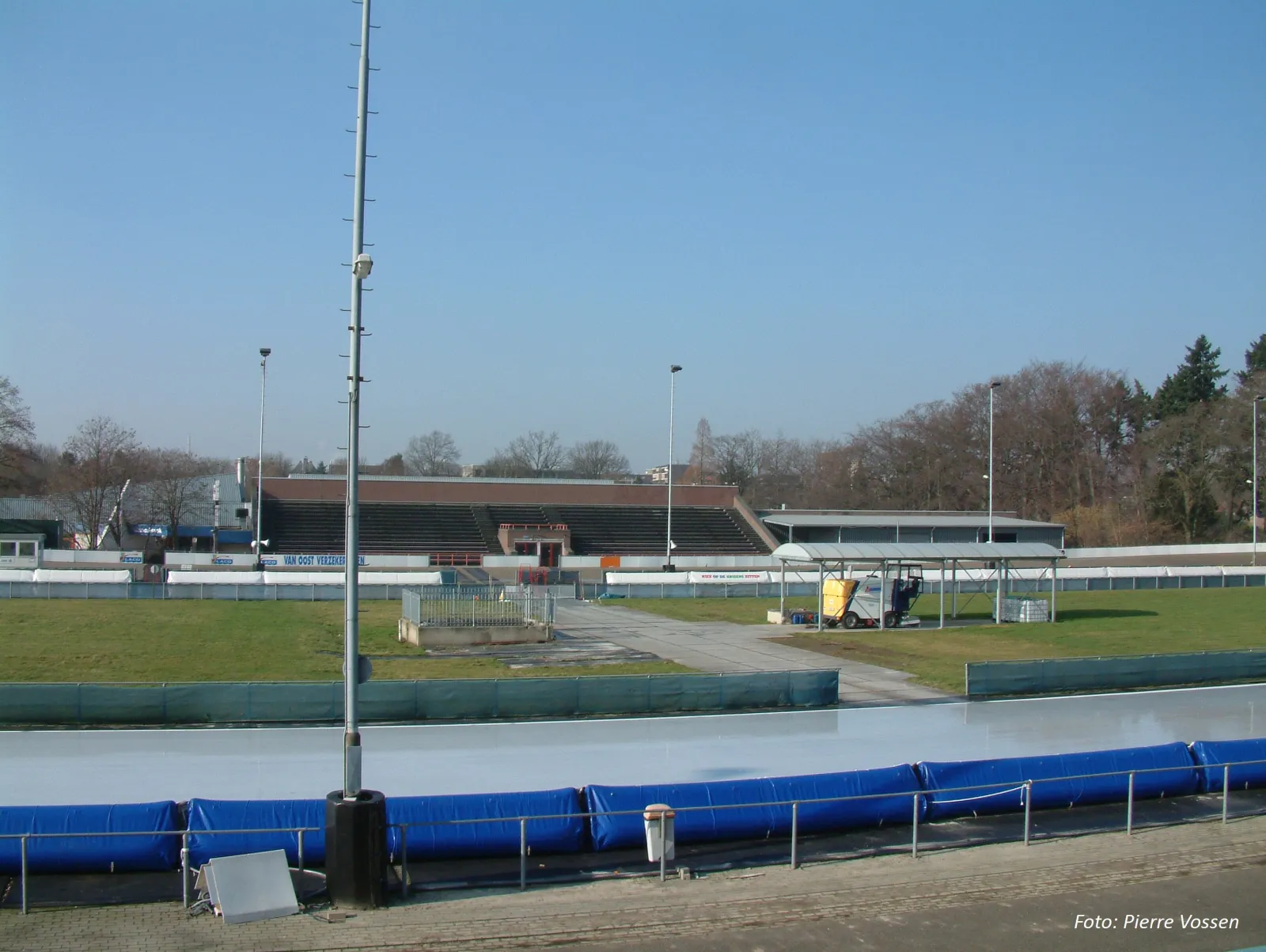 The outdoor 400 m skating oval at Glanerbrook in Geleen with its blue padded track edge, the grandstand and the pavilion behind it — Schaatsbaan Glanerbrook