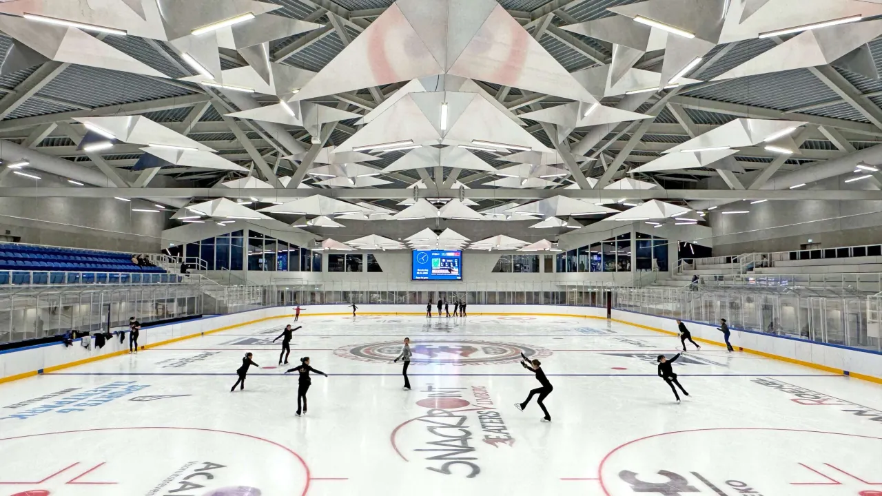 The multifunctional ice floor at Schaatsbaan Glanerbrook with a group of skaters spread across the ice under the folded white metal ceiling, stands and a scoreboard at the far end — Schaatsbaan Glanerbrook