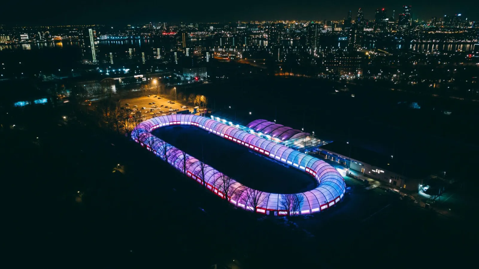 Aerial view at night of the covered 400 metre track at Schaatsbaan Rotterdam, lit in colour — Schaatsbaan Rotterdam