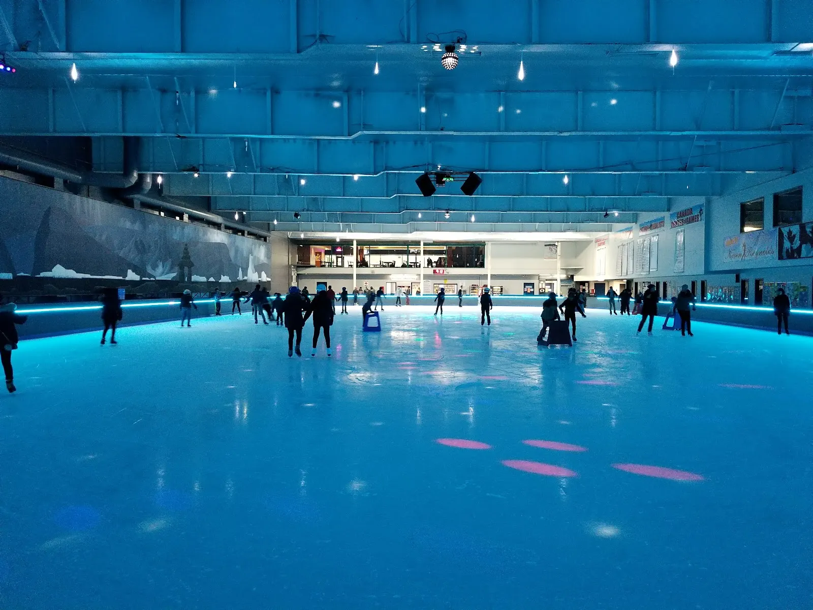 The ice sheet at Scotia Barn lit in blue, seen from the boards, with skaters spread across the far side during a public session — Scotia Barn