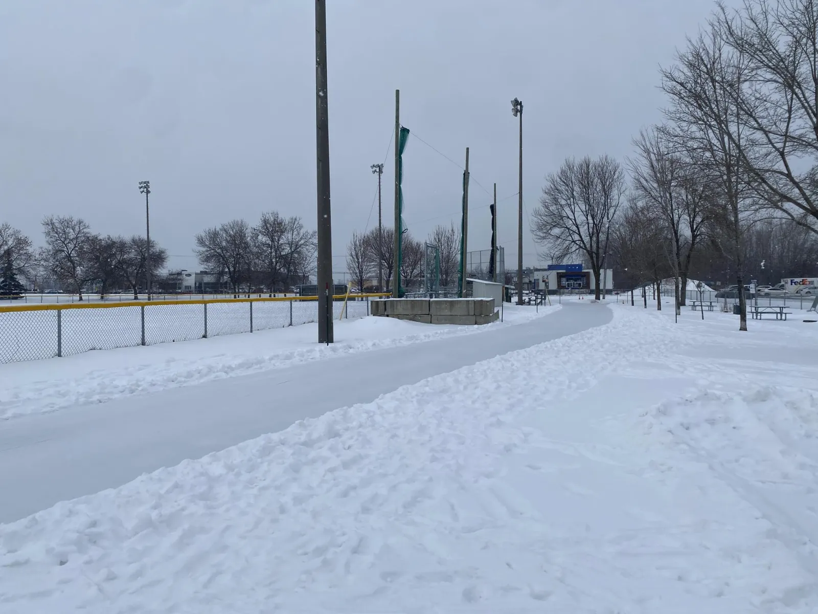 The ice trail of the parc Laviolette in Trois-Rivières in winter, winding past the ball field fence — Sentier glacé du parc Laviolette