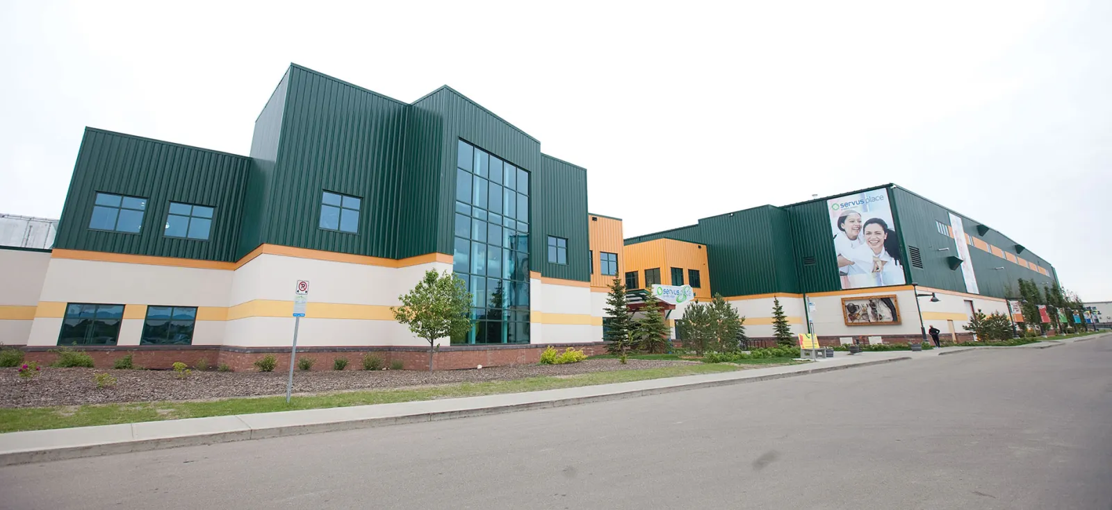 Servus Credit Union Place from the street: green-roofed glass towers over cream walls, with the long arena wing beyond. — Servus Credit Union Place
