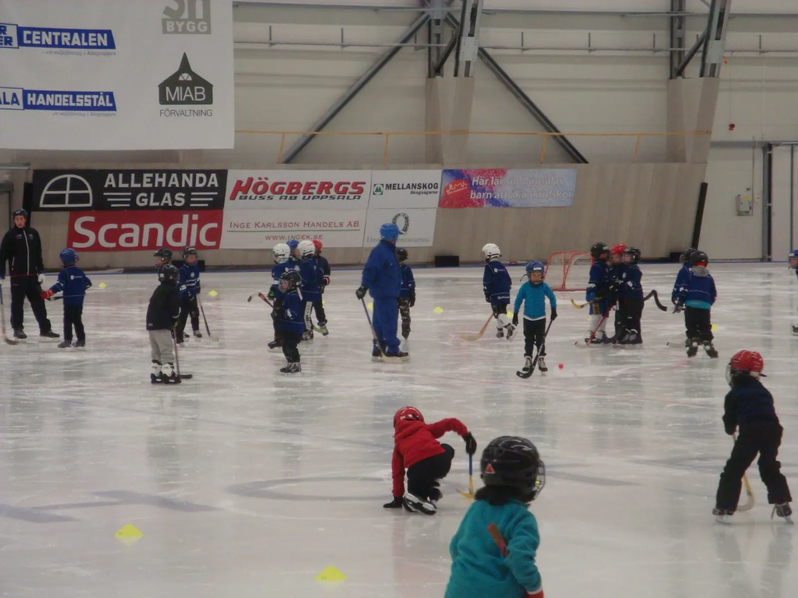 Young skaters in a lesson on the ice of the Serwent hall, sponsor boards along the wall behind them. — Serwenthallen