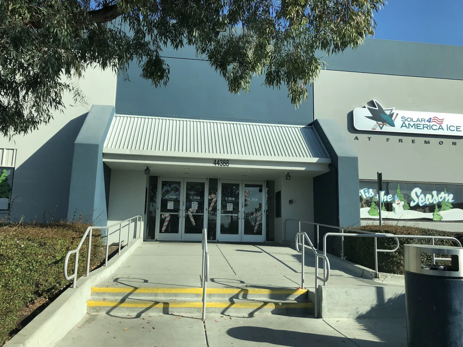 The grey building's glass entrance under a white awning, with a Solar4America Ice sign and the San Jose Sharks logo on the wall. — Sharks Ice at Fremont