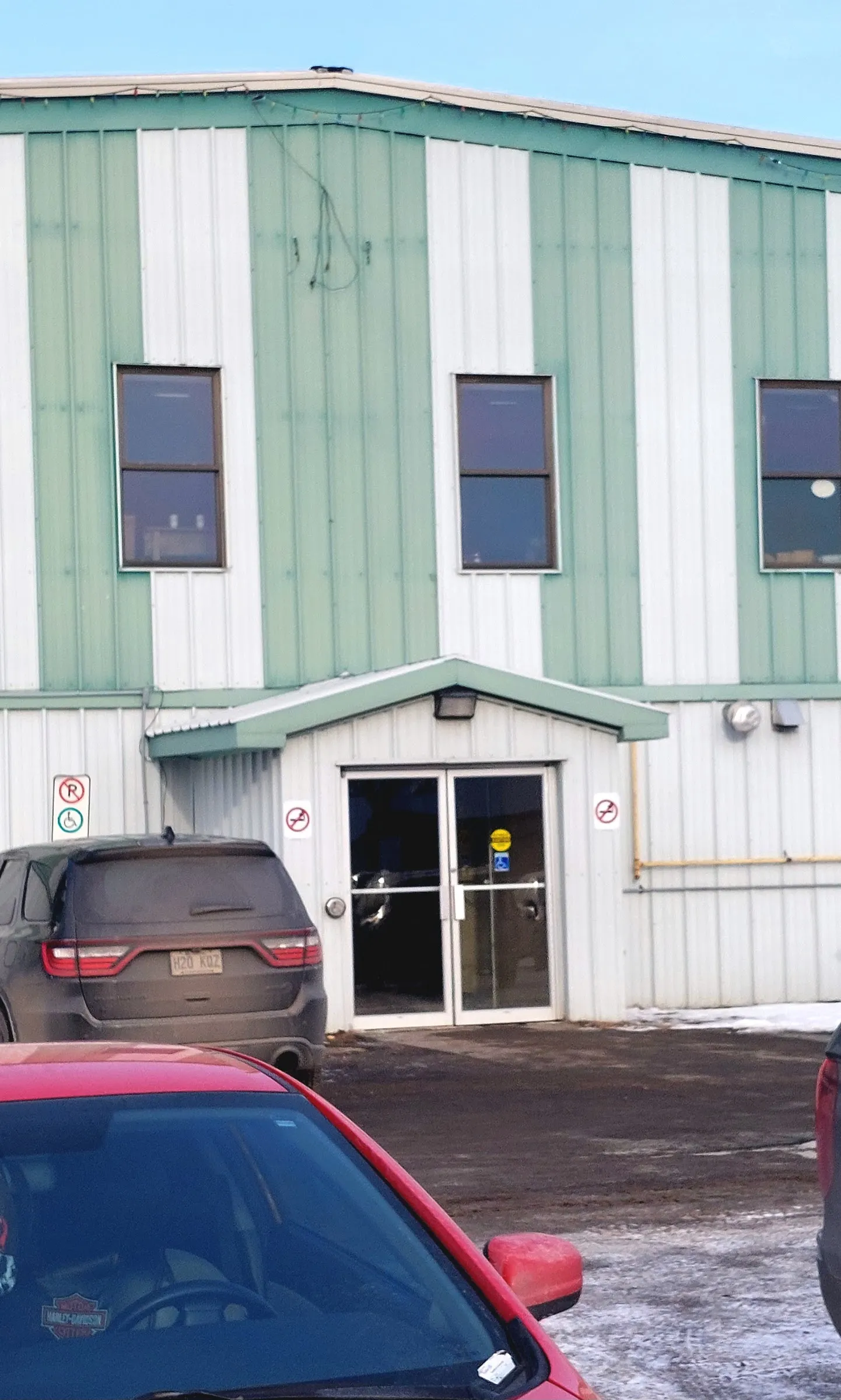 The green and white steel front of the Shawville Arena with its entrance doors and accessible parking sign in winter — Shawville Arena