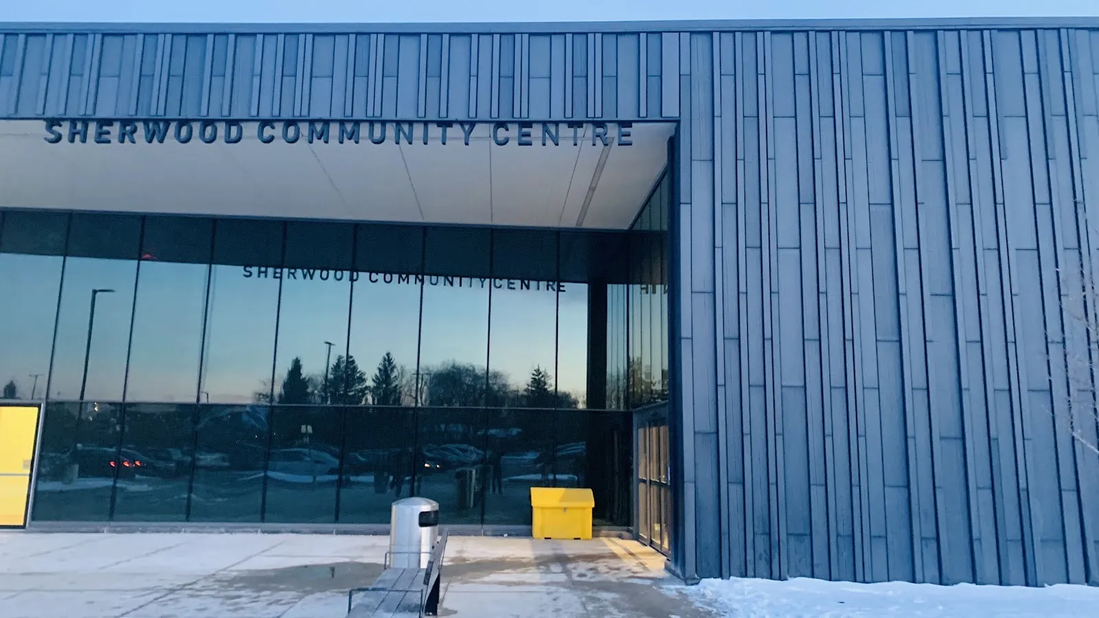 The Sherwood Community Centre entrance, its name lettered over a tall glass front set in dark vertical metal cladding, snow at the edge. — Sherwood Community Centre