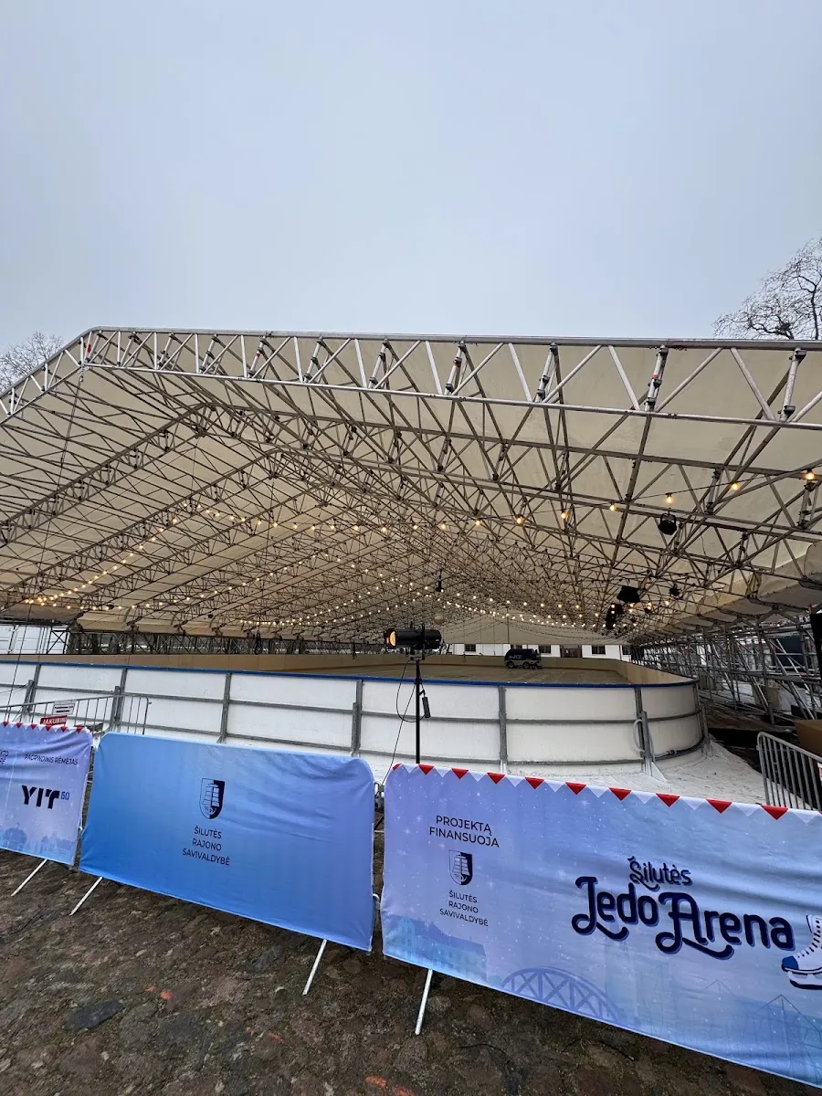 The roofed Šilutės ledo arena rink with its boards and sponsor banners in the Hugo Šojaus dvaras courtyard – Šilutės ledo arena